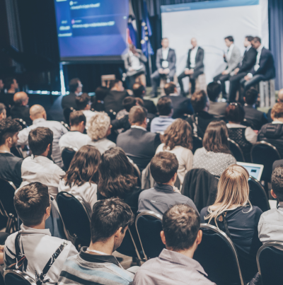 A stock image of a conference hall with speakers and attendees