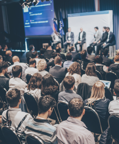 A stock image of a conference hall with speakers and attendees