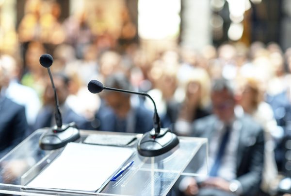 Microphones in focus at business conference, corporate presentation, workshop, coaching training, news conference, company meeting, public or political event. Public speaking concept.